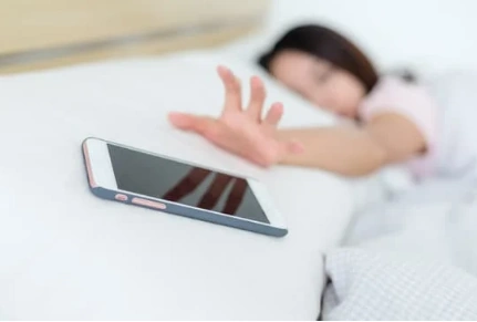 person in bed reaching for their cell phone