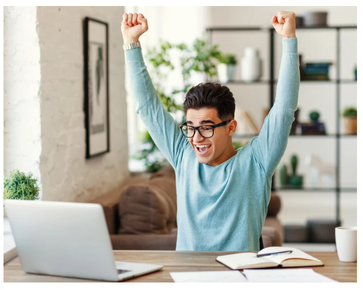 man at computer holding hands up in the air